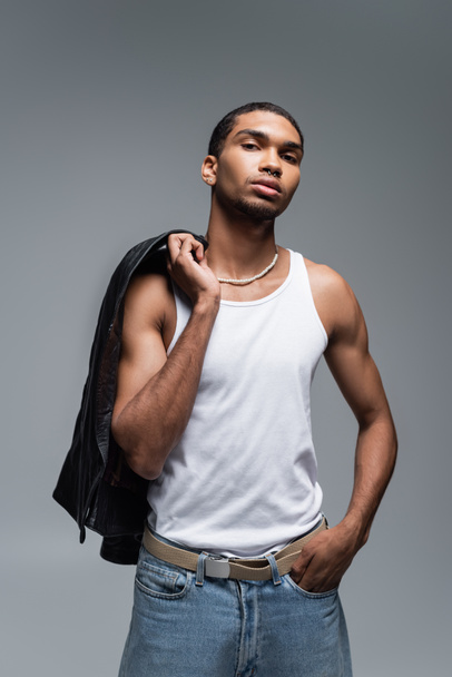 muscular young african american man in tank top holding leather jacket isolated on grey  - Valokuva, kuva
