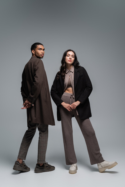 full length of stylish interracial models in trendy autumnal outfits posing together on grey - Fotoğraf, Görsel