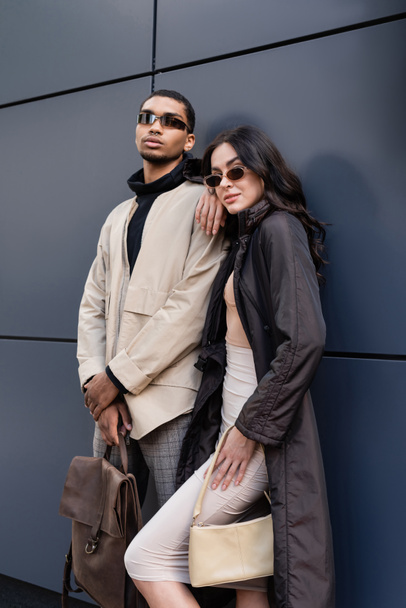 african american man in sunglasses holding leather backpack near stylish woman and building  - Foto, imagen