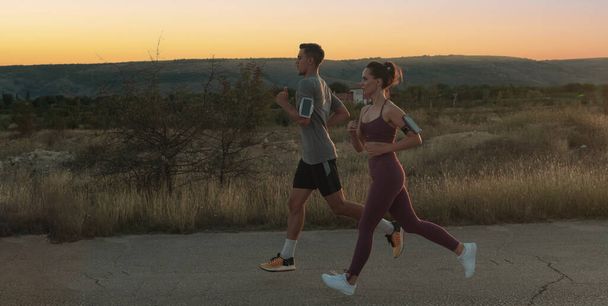 healthy young couple jogging in the city streets in the early morning with a beautiful sunrise in the background. High quality photo - Photo, Image