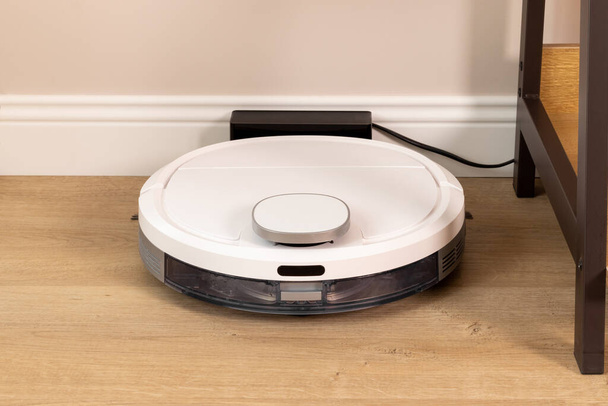 Modern white robot vacuum cleaner based on wooden floor - Foto, Imagen