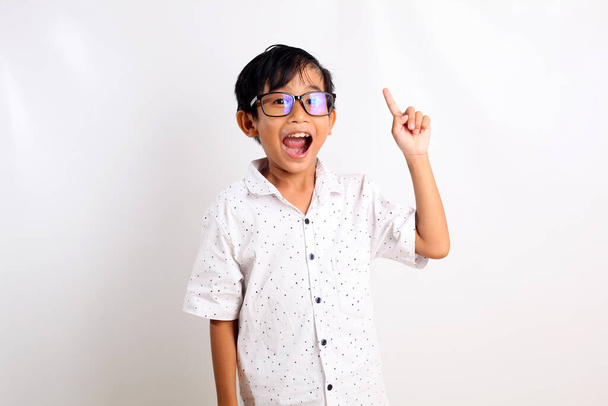 Чарівний азіатський хлопчик в окулярах стоїть, отримуючи ідею і вказуючи пальцем
. - Фото, зображення