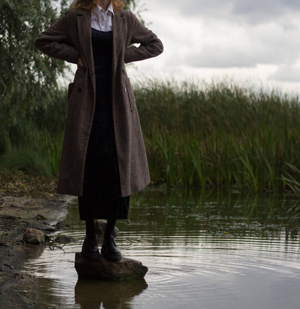 Ένα κορίτσι με παλτό στέκεται κοντά στο ποτάμι το φθινόπωρο. - Φωτογραφία, εικόνα