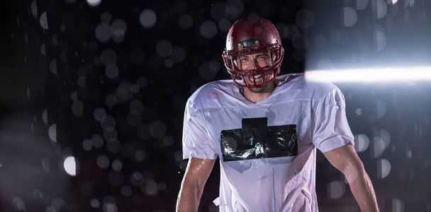 American Football Athlete Warrior Debout sur un terrain tient son casque et prêt à jouer. Joueur se préparant à courir, attaquer et marquer Touchdown. Nuit pluvieuse avec éruption de lentille dramatique et gouttes de pluie. Haut - Photo, image