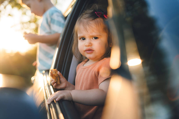 Милі двоє маленьких дітей розважаються, щоб подорожувати на машині і дивитися з вікна автомобіля в сільській місцевості, в той час як їдять свої закуски. Щаслива сім'я
 - Фото, зображення