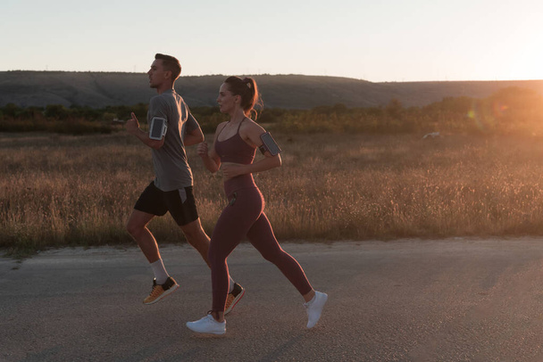 healthy young couple jogging in the city streets in the early morning with a beautiful sunrise in the background. High quality photo - Foto, immagini