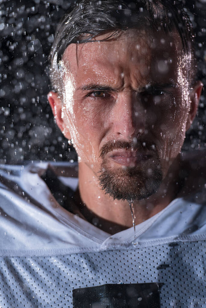 American Football Athlete Warrior Standing on a Field Holds his Helmet and Ready to Play. Player Preparing to Run, Attack and Score Touchdown. Rainy Night with Dramatic lens flare and rain drops. High - Foto, immagini