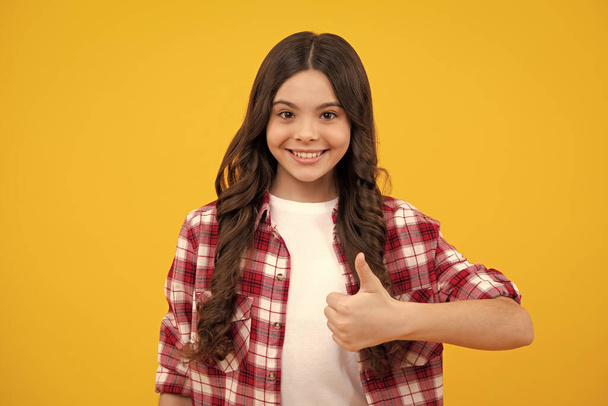 Teenager child girl 12, 13, 14 year old doing thumbs up gesture. Cheerful teenager girl showing thumbs up sign, isolated on yellow background. Happy teenager, positive and smiling emotions. - Valokuva, kuva