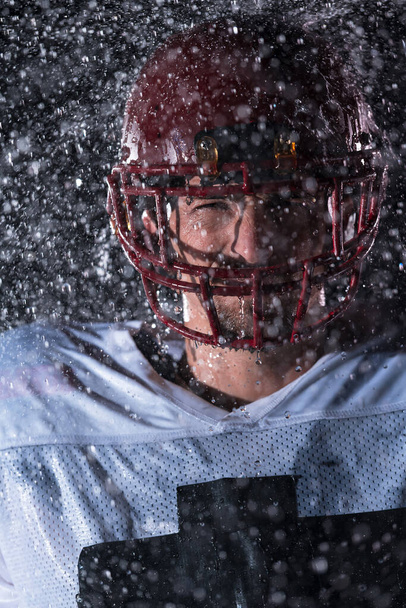 American Football Athlete Warrior Standing on a Field Holds his Helmet and Ready to Play. Player Preparing to Run, Attack and Score Touchdown. Rainy Night with Dramatic lens flare and rain drops. High - Foto, Imagen