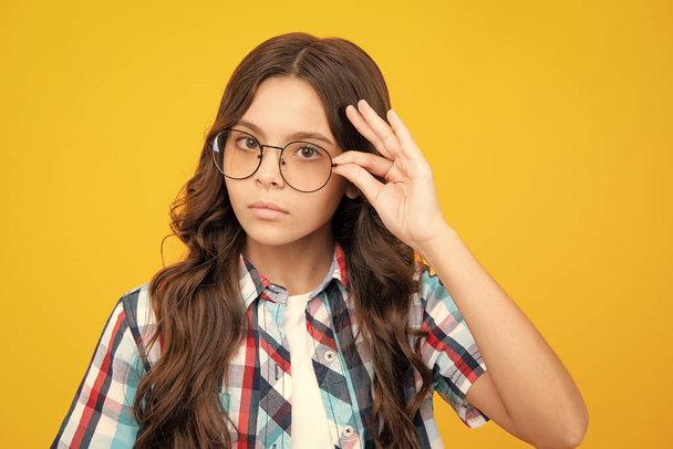 Headshot portret van schattige tiener kind meisje geïsoleerd op gele studio achtergrond slijtage bril kijken camera, kind proberen bril op opticiens, kind gezichtsvermogen behandeling concept - Foto, afbeelding