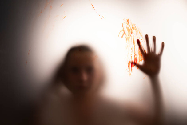 Horror ghost girl with blood on her hand behind the matte glass. Halloween festival concept. - Foto, afbeelding