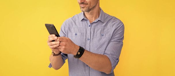 Ευκίνητη δουλειά. Όμορφος άντρας με ασύρματα ακουστικά. επιχειρηματίας χρησιμοποιεί ακουστικά. trendy άνδρες σε κίτρινο φόντο. εξάρτημα συσκευής ακουστικών. νέα τεχνολογία. επιτυχημένος αξύριστος τύπος χρησιμοποιούν smartphone. - Φωτογραφία, εικόνα