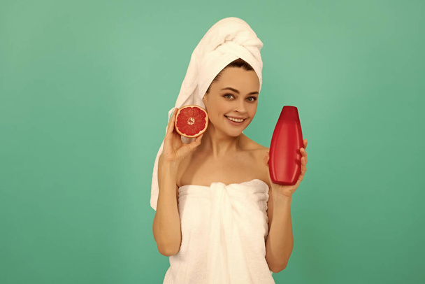 glückliche Frau im Handtuch mit Grapefruit-Shampoo-Flasche auf blauem Hintergrund. - Foto, Bild