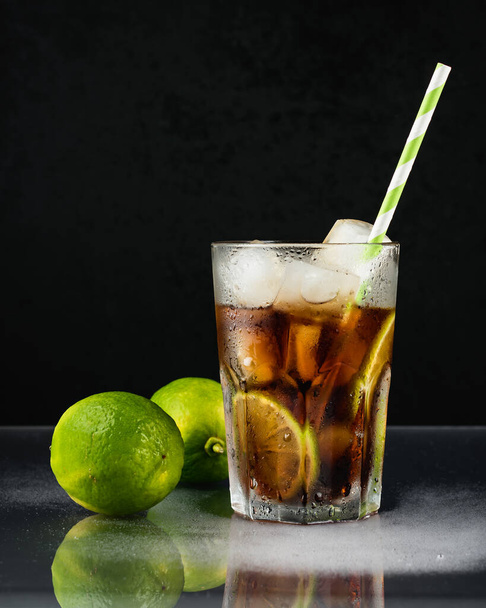Cuba libre cocktail met limoen op een zwarte achtergrond. - Foto, afbeelding