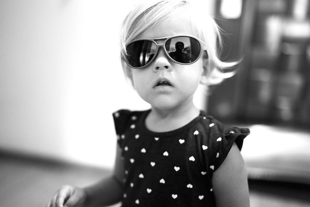 Маленька дівчинка в сонцезахисних окулярах і точковій сукні. Чорно-біле фото. Високоякісна фотографія
 - Фото, зображення
