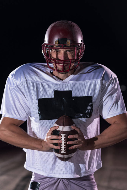 American Football Athlete Warrior Standing on a Field Holds his Helmet and Ready to Play. Player Preparing to Run, Attack and Score Touchdown. Rainy Night with Dramatic lens flare and rain drops. High - Photo, Image