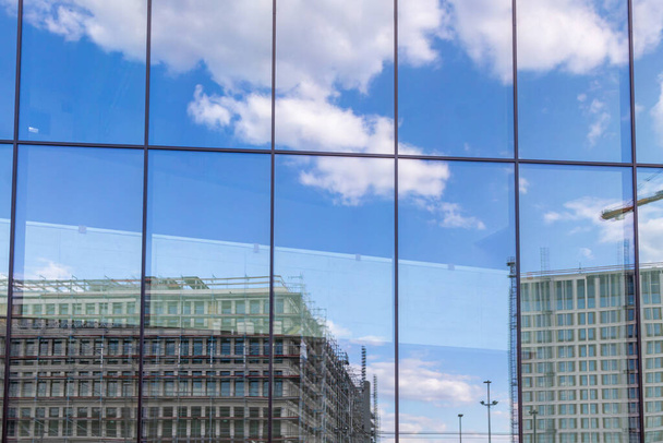 Reflexão de um grande canteiro de obras com novos edifícios e céu ligeiramente nublado numa fachada de vidro de um edifício moderno - Foto, Imagem