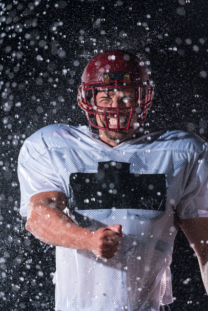 American Football Athlete Warrior Standing on a Field Holds his Helmet and Ready to Play. Player Preparing to Run, Attack and Score Touchdown. Rainy Night with Dramatic lens flare and rain drops. High - Foto, afbeelding