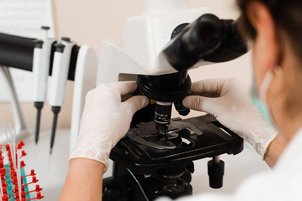 Laboratorioassistentti tutkii mikroskooppia ja tekee verikokeen laboratoriossa. Lääketieteelliset laitteet hematologisia ja biokemiallisia verikokeita varten klinikalla - Valokuva, kuva