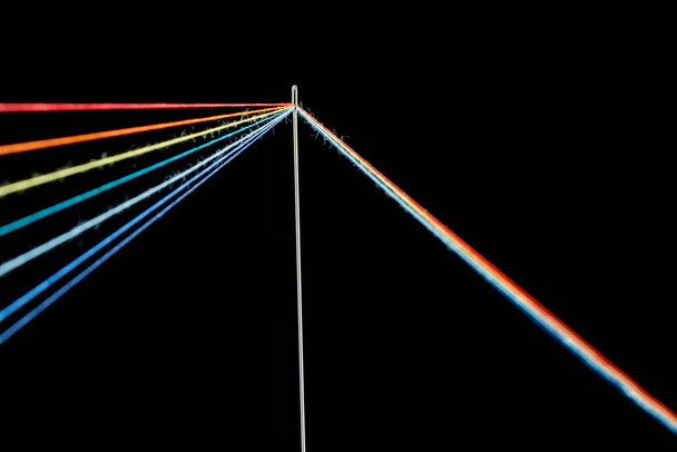 multi-colored threads for sewing in the form of a rainbow pass through an antique needle on a black background close-up - Photo, Image
