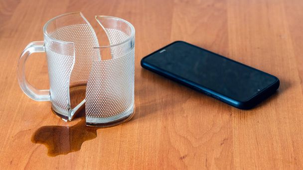 Kaputte Tasse und Handy, Smartphone, im Büro auf einem Holztisch - Foto, Bild