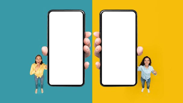 Collage de dos mujeres que muestran enormes teléfonos con pantallas en blanco Publicidad aplicación móvil sobre fondo de estudio amarillo y azul. Gran App Publicidad Concepto. Mockup, Panorama, Vista superior - Foto, imagen