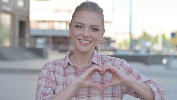 Loving Casual Woman showing Heart Shape by Hands Outdoor - Photo, image