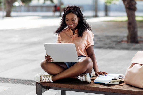 technologie, vzdělávání a lidé koncept - šťastný usměvavý africký americký student dívka s notebookem a knihy ve městě - Fotografie, Obrázek