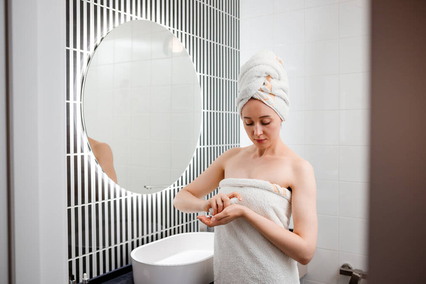 Молодая женщина наносит крем от морщин, стоящий за зеркалом в домашней ванной. Косметология и косметика. Уход за кожей после очищения - Фото, изображение