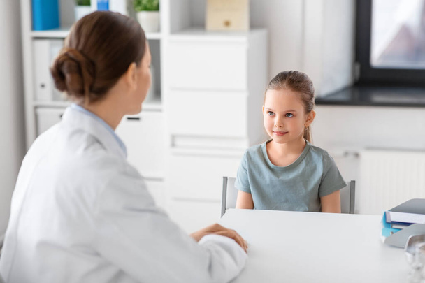 medicine, healthcare and pediatry concept - female doctor or pediatrician talking to little girl patient on medical exam at clinic - 写真・画像
