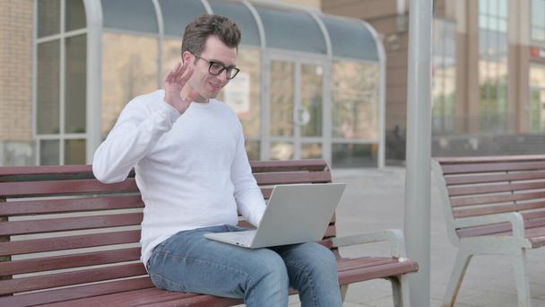 Casual Man Talking on Video Call while Sitting Outdoor on Bench - Foto, Imagen