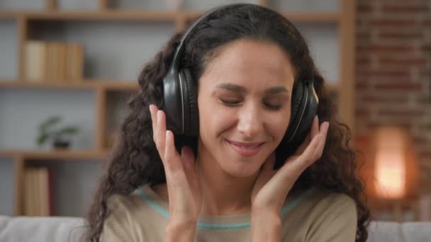 Front view close up smiling Hispanic woman with smiling enjoining lady relaxing at home with closed eyes listening to music in headphones audio sound song feeling well good mood hobby holiday indoors - Video
