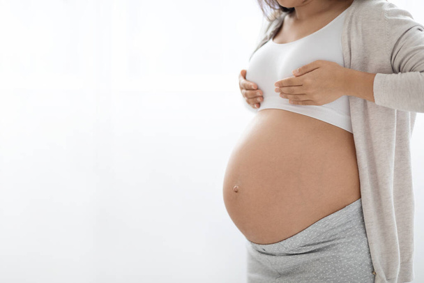 Unrecognizable young pregnant woman with big tummy having painful feelings in breast, massaging herself, cropped photo, white background, panorama with copy space - Photo, Image