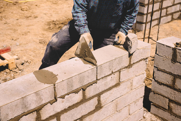 Professional construction worker laying bricks and mortar - building external house walls. Construction site detail -closeup of hand adjusting bricks - Photo, image