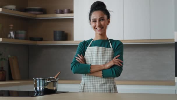 Wesoła piękna kobieta nosi fartuch stojący w nowoczesnej kuchni z skrzyżowanymi rękami uśmiechnięta szczęśliwa gospodyni domowa kucharz piekarz patrząc na aparat gotowanie pyszne jedzenie śniadanie pozowanie w kuchni wnętrza - Materiał filmowy, wideo