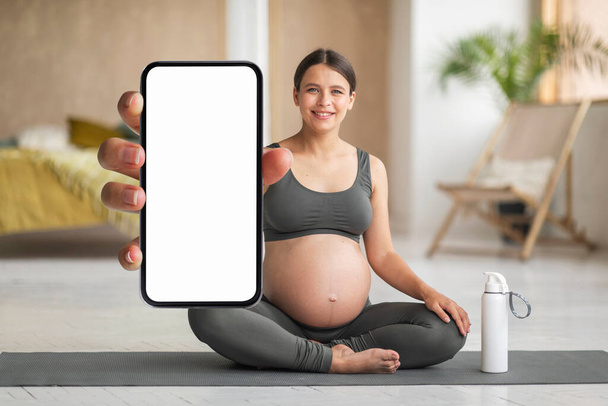 Happy Young Pregnant Woman Practicing Yoga At Home And Demonstrating Blank Smartphone With White Screen, Smiling Expectant Female Showing Empty Cellphone For App Or Website Design, Mockup - Foto, Imagem