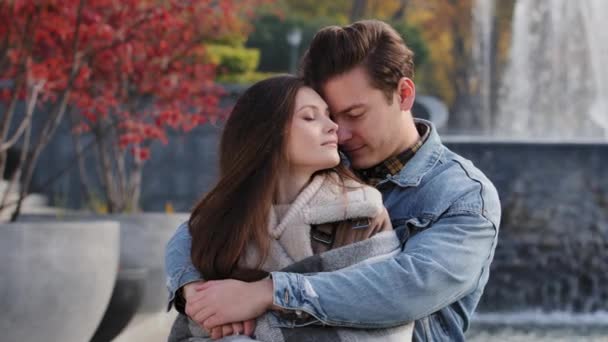Caucasian couple lovers partners stand background of city fountain pressed closely to cheeks together spend time in autumn park on date embrace feel love emotion romantic atmosphere happy young family - Footage, Video