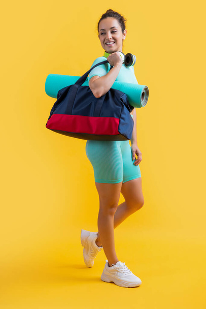 smiling fitness woman in sportswear with sport bag in studio. fitness woman in sportswear isolated on yellow background. fitness and sportswear. - Fotó, kép