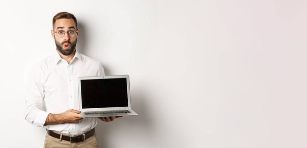 Amazed businessman showing laptop screen, standing against white background. - Valokuva, kuva