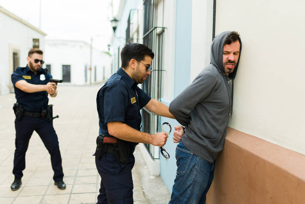 Zły złodziej stawiający opór przy aresztowaniu i glina zakładający kajdanki po zatrzymaniu za popełnienie przestępstwa - Zdjęcie, obraz