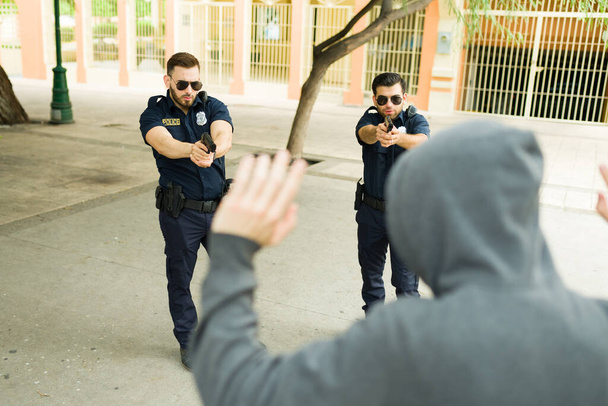 Tylny widok złodzieja podnoszącego ręce podczas aresztowania przez policjantów celujących w broń po popełnieniu przestępstwa. - Zdjęcie, obraz
