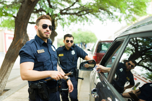 Atractivos agentes de policía mirando a la cámara mientras un conductor intenta sobornarlos con dinero para una multa por exceso de velocidad - Foto, Imagen