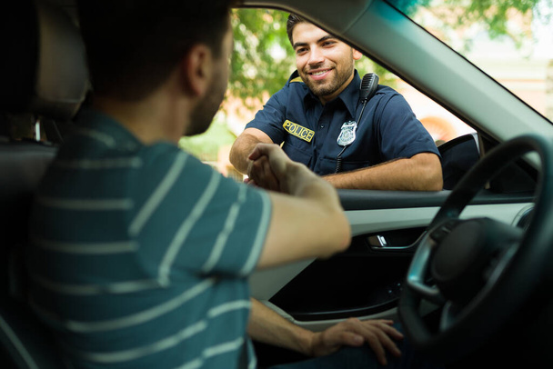 Mutlu polis memuru biraz yardım aldıktan sonra el sıkışıyor ve sürücüye gülümsüyor. - Fotoğraf, Görsel