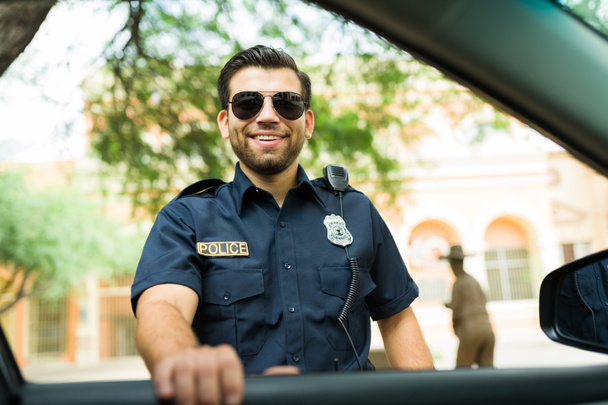 Χαρούμενος αστυνομικός πράκτορας χαμογελά και κάνει οπτική επαφή, ενώ μιλάει με έναν οδηγό  - Φωτογραφία, εικόνα