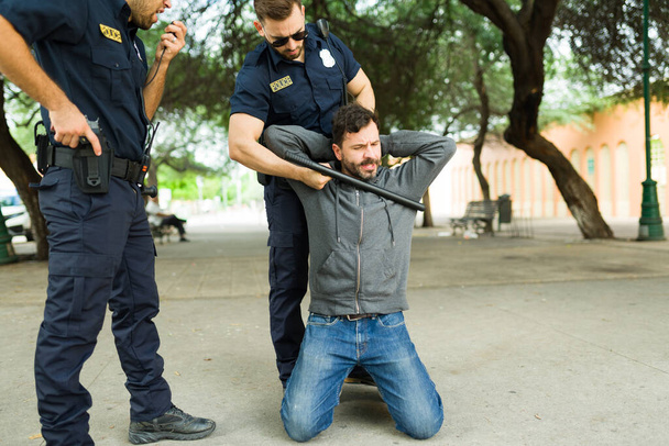 Polizeibeamte nehmen einen aufgebrachten kaukasischen Mann oder Kriminellen auf Knien fest  - Foto, Bild
