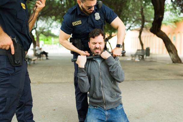 Θυμωμένος νεαρός άνδρας εγκληματίας που αντιστέκεται στη σύλληψη ενώ προσπαθεί να δραπετεύσει από τους αστυνομικούς και να πολεμήσει έναν αστυνομικό χρησιμοποιώντας ένα γκλομπ - Φωτογραφία, εικόνα