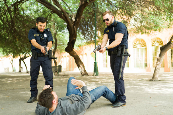 Wütende Polizisten rufen einem Mann auf dem Boden zu, der nach einem Raubüberfall seine Waffe auf einen Tatverdächtigen richtet  - Foto, Bild