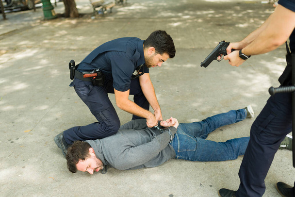 警官は暴力的な若い男の犯罪者に手錠をかけ屋外で逮捕する - 写真・画像