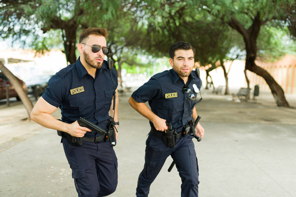 Agenti di polizia attraenti in uniforme nera che corrono e inseguono un sospetto criminale per strada - Foto, immagini