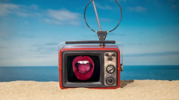 Een vintage televisie op het strand met glitch bewegende rode lippen op het scherm - Video